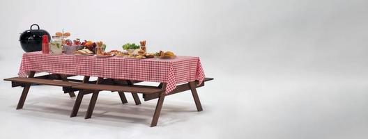 Picnic table and red checkered tablecloth with food and drink for outdoor party. Isolated photo
