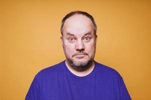 mid adult man with dumbfounded look on his face against orange color studio background photo