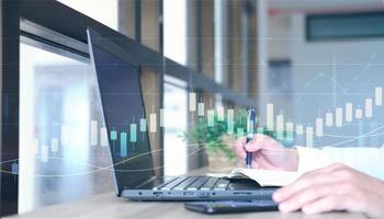 Concept of international internet trading is represented by a double exposure of graphs and financial data, as well as a workplace with a computer background photo