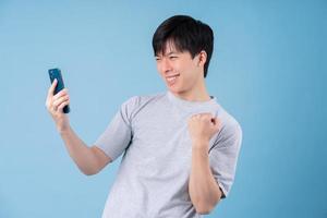 Young Asian man using smartphone on blue background photo