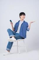joven asiático sentado y usando un teléfono inteligente con fondo blanco foto