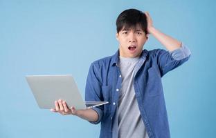 Young Asian man using laptop on blue background photo