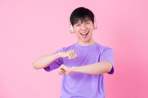 Young Asian man listening music on pink background photo