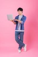 Young Asian man standing and using laptop on pink background photo