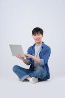 Young Asian man sitting and using laptop on white background photo