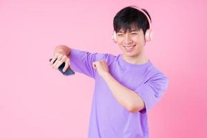 Young Asian man listening music on pink background photo