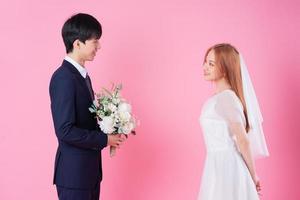 Young Asian bride and groom posing on pink background photo