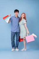 Young Asian couple carrying shopping bag on blue background photo