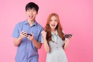 Young Asian couple using smartphone on pink background photo