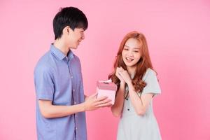 Young Asian couple holding pink gift box on pink background photo