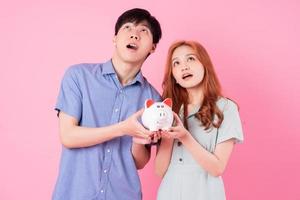 Young Asian couple holding piggy bank on pink background photo