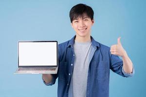 Young Asian man using laptop on blue background photo