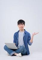 Young Asian man sitting and using laptop on white background photo