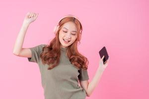 Young Asian woman using smartphone and listening music on pink background photo