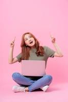 Young Asian woman sitting and using laptop on pink background photo