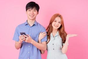 Young Asian couple using smartphone on pink background photo