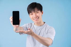 Young Asian man using smartphone on blue background photo