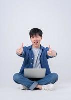 Young Asian man sitting and using laptop on white background photo