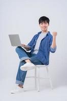 Young Asian man sitting and using laptop on white background photo