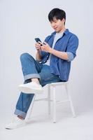 Young Asian man sitting and using smartphone on white background photo