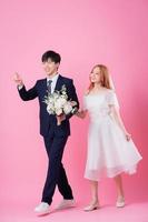 Young Asian bride and groom posing on pink background photo