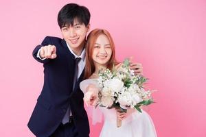 Young Asian bride and groom posing on pink background photo