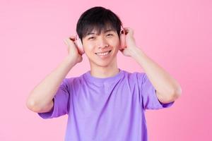 Young Asian man listening music on pink background photo