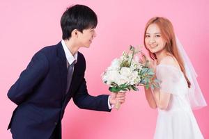 Young Asian bride and groom posing on pink background photo
