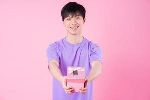 Young Asian man holding pink giftbox on pink background photo