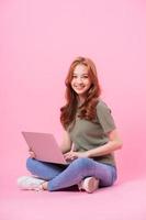 joven asiática sentada y usando una laptop con fondo rosa foto