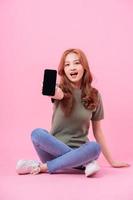Young Asian woman sitting and using smartphone on pink background photo