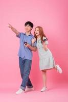 Young Asian couple using smartphone on pink background photo