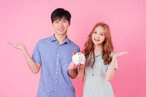 Young Asian couple holding piggy bank on pink background photo