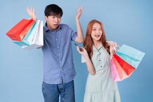 Young Asian couple carrying shopping bag on blue background photo