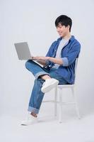 Young Asian man sitting and using laptop on white background photo