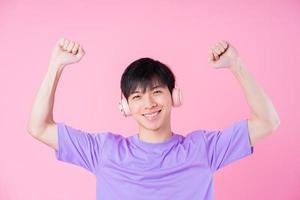 Young Asian man listening music on pink background photo