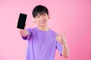 Young Asian man listening music on pink background photo