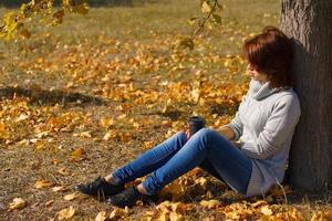 hermosa chica en el bosque de otoño. una mujer se sienta cerca de un árbol en un parque de otoño foto