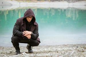 Young man in glasses and vest with a hood on the background of a turquoise lake photo