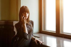 una mujer joven se para en la ventana hablando por teléfono foto