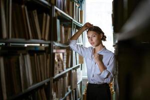 Beautiful female student  stands between the rows in the library, photo