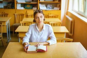 a young woman sitting at a Desk in a white shirt, a book on the table, a beautiful student photo