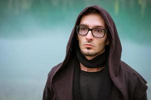 Young man in glasses and vest with a hood on the background of a turquoise lake photo