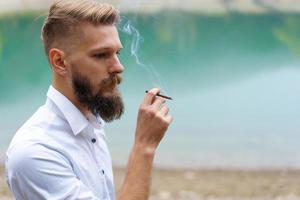 Young man beard smokes cigarette or tobacco. Guy is addicted to cigarettes photo