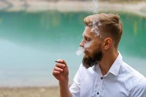 Handsome serious guy, young thoughtful man smokes, heating tobacco products photo