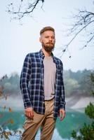 Young caucasian bearded man in plaid shirt traveling alone in autumn forest photo