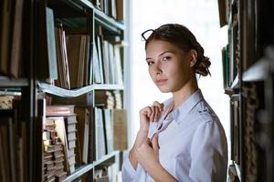 hermosa estudiante se encuentra entre las filas de la biblioteca, foto