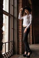 a young woman in a hat standing at the window, posing for the camera photo