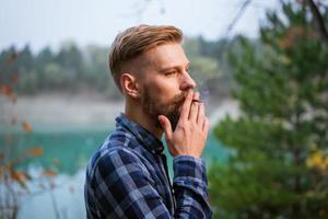 The bearded man smokes. Handsome stylish man in plaid shirt with cigarette. photo