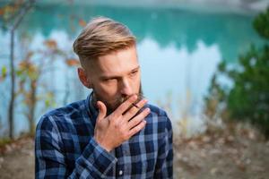 The bearded man smokes. Handsome stylish man in plaid shirt with cigarette. photo